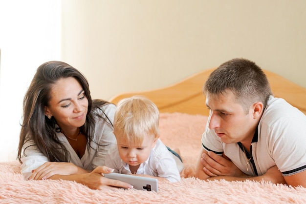 Famiglia felice sdraiata sul letto guardando il telefono mamma papà e figlio piccolo