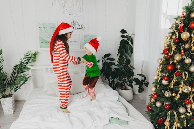 Famiglia felice sorella e fratello in pigiama che saltano a letto la mattina di natale