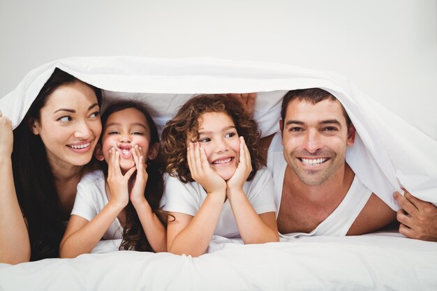 Famiglia felice sotto la coperta sul letto a casa