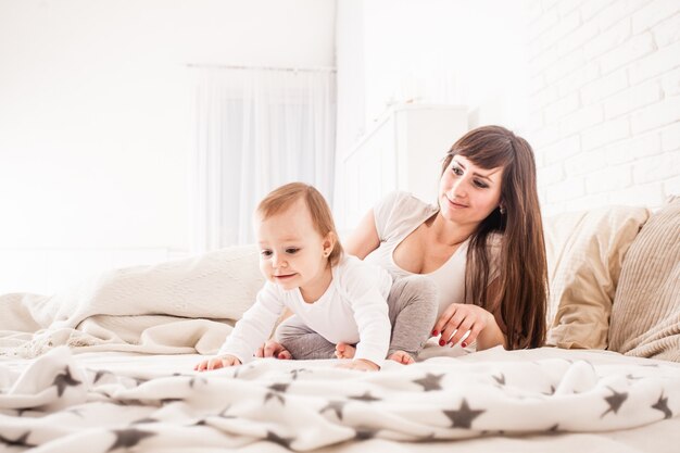 Famiglia felice sul letto. Madre e altro giocano con la loro bambina. Interni bianchi e chiari in camera da letto, ora del mattino