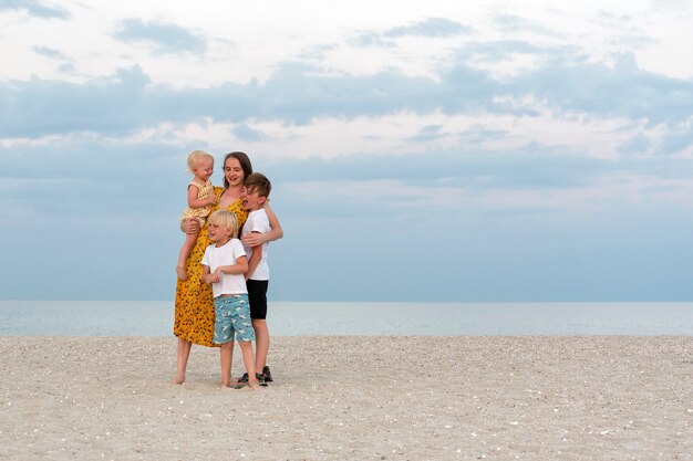 Famiglia felice sulla spiaggia. Mamma e tre bambini che si divertono sul mare. Stile di vita familiare.