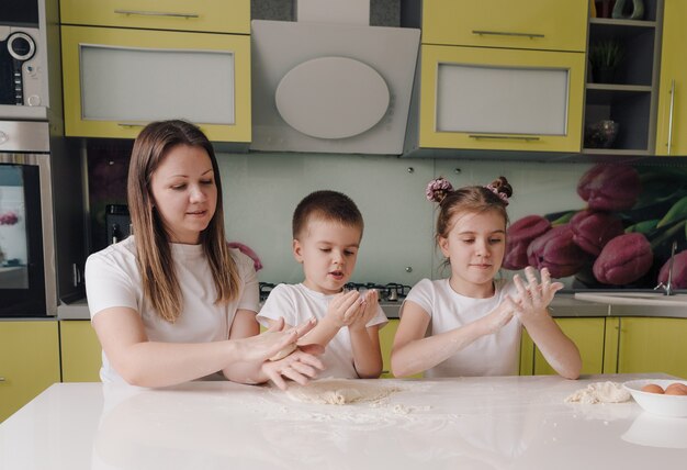 Famiglia felice una madre e due bambini piccoli imparano a fare la pasta in una cucina domestica