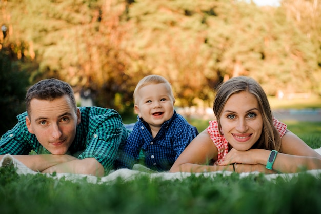 Famiglia felice vestita con le camicie a scacchi sdraiato sul plaid nel parco e guardando la fotocamera