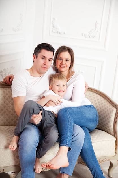 Famiglia in bianco e jeans sul divano leggero contro il muro bianco