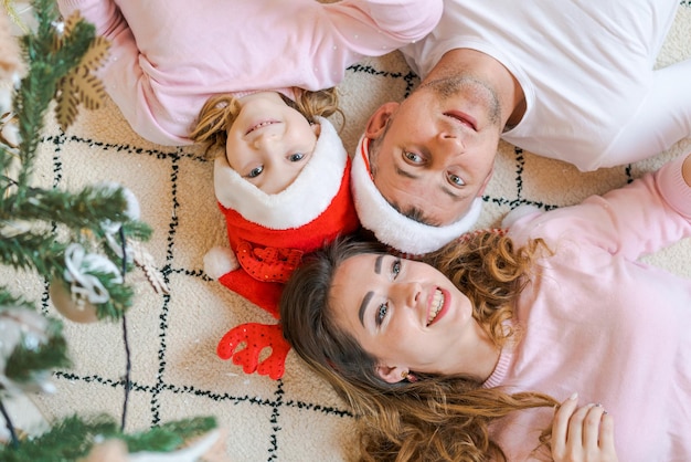 Famiglia in cappelli di Babbo Natale con la figlia in abiti leggeri e comodi sdraiati