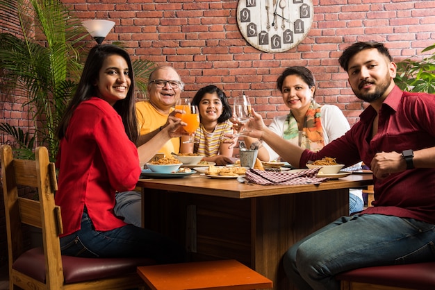 Famiglia indiana che mangia cibo al tavolo da pranzo a casa o al ristorante mangiando insieme