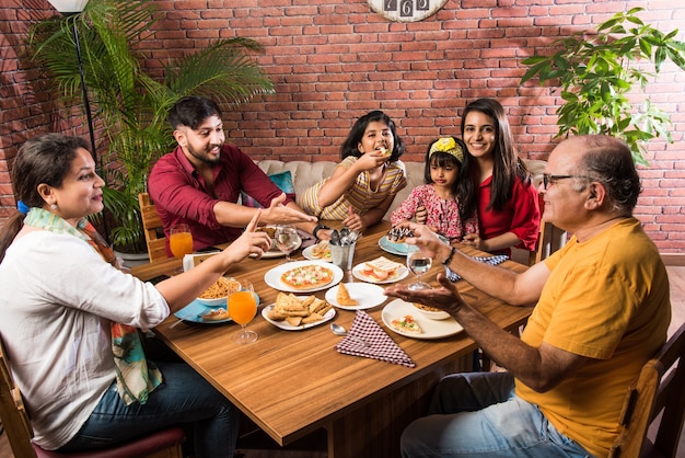 Famiglia indiana che mangia cibo al tavolo da pranzo a casa o al ristorante mangiando insieme