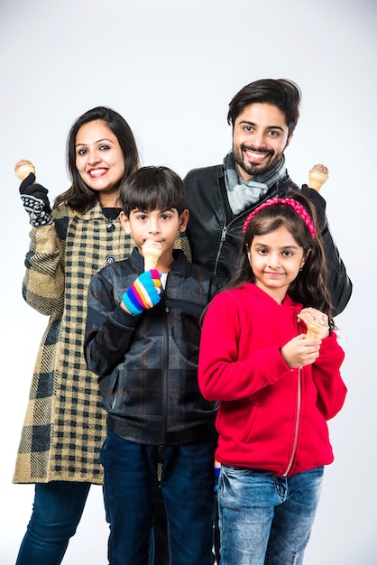 Famiglia indiana che mangia il gelato in vestiti caldi su fondo bianco