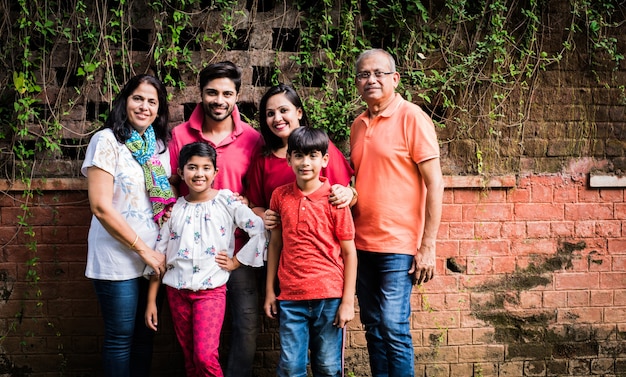 Famiglia indiana in fila contro il muro ricoperto di rampicanti. Multi generazione di famiglie asiatiche nel parco o in giardino che si divertono, sano concetto di vita familiare