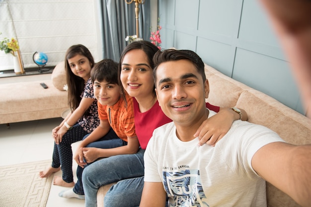 Famiglia indiana seduta sul divano e scattando foto selfie usando lo smartphone