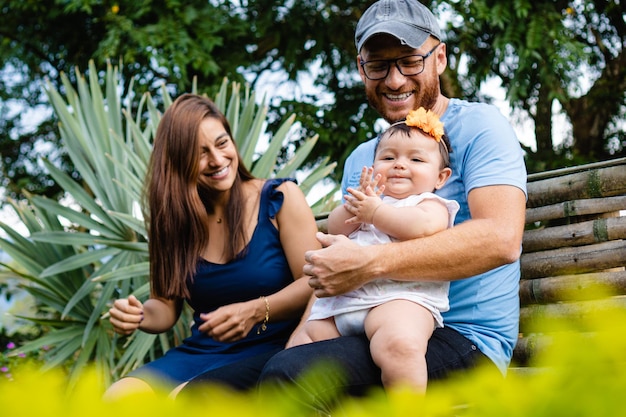 Famiglia latina sorridente con una neonata in grembo seduta in un parco