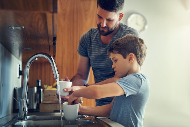 Famiglia lavare i piatti e la pulizia con padre figlio e attrezzature con batteri panno e tazze faccende d'appartamento e papà con ragazzo genitore single e insegnamento con le persone apprendimento e pulizia domestica