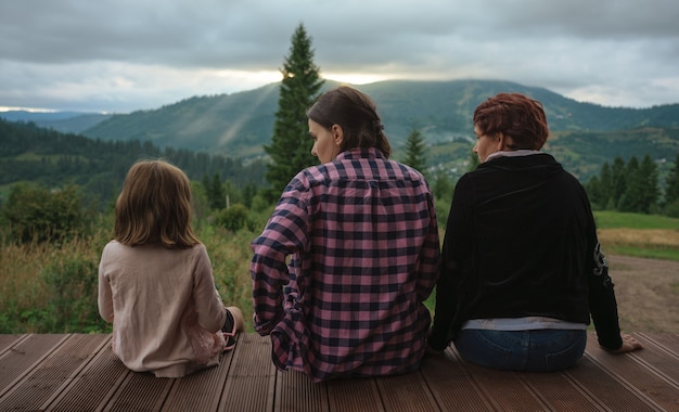 Famiglia LGBT con bambina seduta all'aperto sulla terrazza e guardare il tramonto in montagna