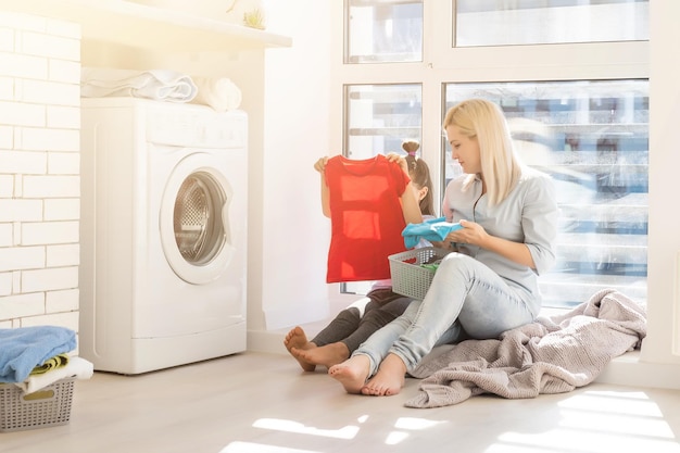 famiglia madre e bambina piccola aiutante nella lavanderia vicino alla lavatrice e ai vestiti sporchi