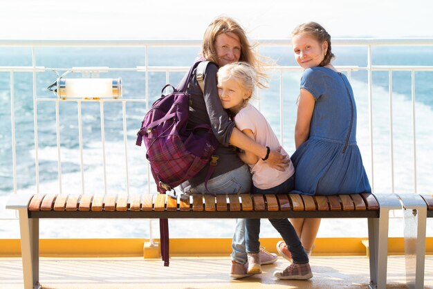 Famiglia - madre e due figlie sedute su una panchina sul traghetto e il mare sullo sfondo