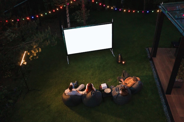 Famiglia madre padre e bambini guardano un film proiettore con popcorn la sera nel cortile