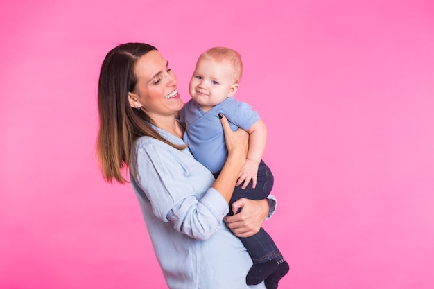 Famiglia, maternità, genitorialità, persone e concetto di assistenza all'infanzia - madre felice tiene adorabile bambino sopra il muro rosa.