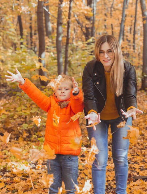 Famiglia monoparentale che gioca con le foglie autunnali nel parco mamma e figlio felici lanciano foglie autunnali dentro