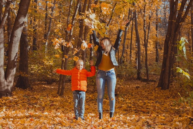 Famiglia monoparentale che gioca con le foglie d'autunno nel parco. Felice mamma e figlio lanciano foglie d'autunno nel parco autunnale.