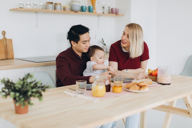 Famiglia multiculturale felice. Papà asiatico e sua moglie bionda caucasica fanno colazione con il loro bellissimo figlio in cucina.