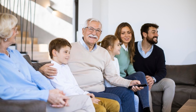 Famiglia multigenerazionale seduta insieme sul divano di una casa moderna e guardando la TV