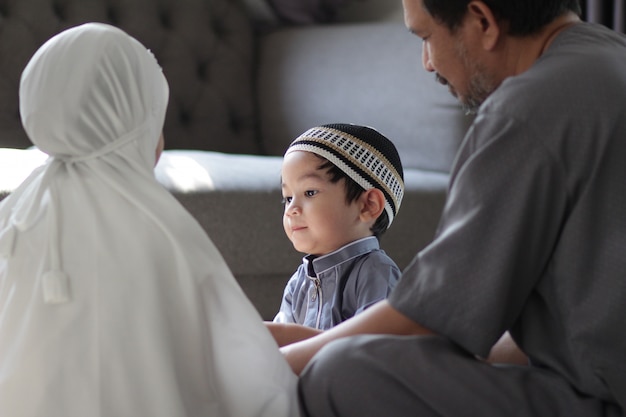 Famiglia musulmana asiatica in costume tradizionale.Padre musulmano con i bambini nella loro casa dopo aver pregato Dio.Concetto di persone musulmane nel mese sacro del Ramadan.