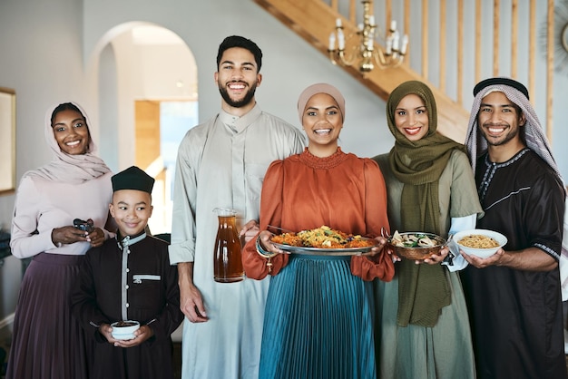 Famiglia musulmana festiva sorridente che celebra il pranzo di festa eid o ramadan insieme tenendo piatti di cibo a casa Felice gruppo di amici di religione islamica tradizionale che si godono le vacanze culturali