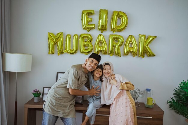 Famiglia musulmana sorridente mentre si siede davanti alla decorazione di eid mubarak