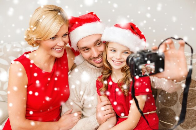 famiglia, natale, natale, inverno, felicità e concetto di persone - famiglia sorridente in cappelli di Babbo Natale che scatta foto con la macchina fotografica