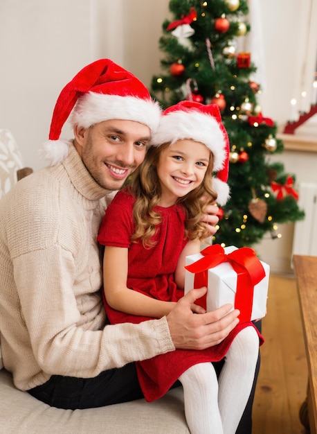 famiglia, natale, natale, inverno, felicità e concetto di persone - padre e figlia sorridenti in cappelli di santa helper che tengono scatola regalo