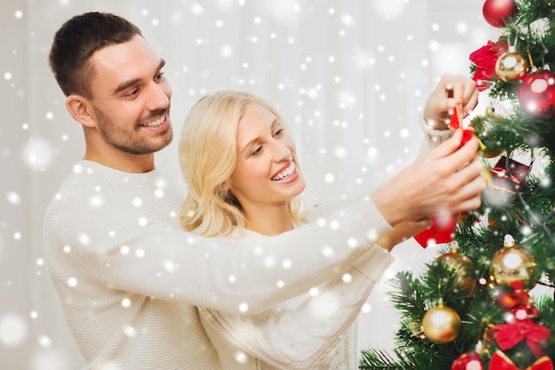 Famiglia, natale, vacanze invernali e concetto della gente - coppie felici che decorano l'albero di Natale a casa