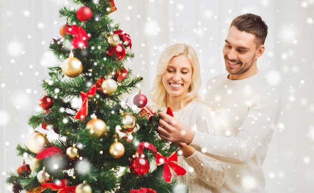 Famiglia, natale, vacanze invernali e concetto della gente - coppie felici che decorano l'albero di Natale a casa