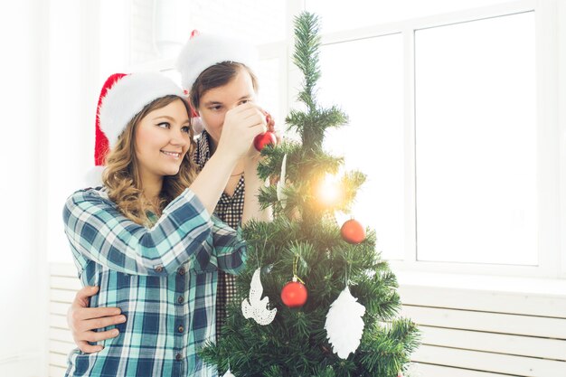 Famiglia, natale, vacanze invernali e concetto di persone - giovani coppie felici che decorano l'albero di natale a casa.