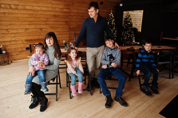 Famiglia nella moderna casa di legno seduta contro il tavolo con albero di Natale che trascorre del tempo insieme in calore e amore