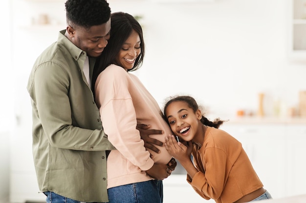 Famiglia nera felice che abbraccia bambino in attesa in cucina a casa