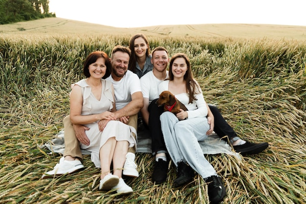 Famiglia numerosa con cinque persone si siede in un campo di grano al tramonto del giorno. abbracci di famiglia felici durante un picnic. vacanza in famiglia per genitori con bambini