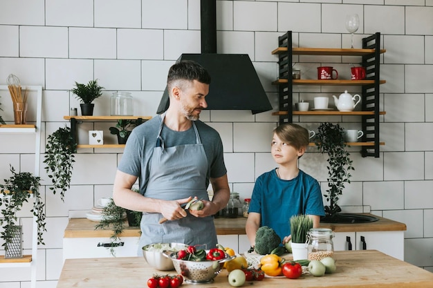 famiglia papà giovane e figlio adolescente cucinano insalata di verdure in cucina e trascorrono del tempo di qualità insieme padre e figlio parlando e cucinando cibo vegetariano e facendo le faccende domestiche 8 marzo e festa della mamma