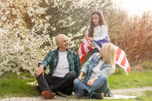 Famiglia patriottica che tiene la bandiera usa all'aperto. Felice coppia caucasica invecchiata che tiene la bandiera usa sullo sfondo verde.