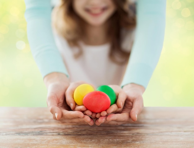 famiglia, persone, vacanze e concezione dell'infanzia - primo piano di una ragazza felice e di una madre con le mani che tengono uova colorate