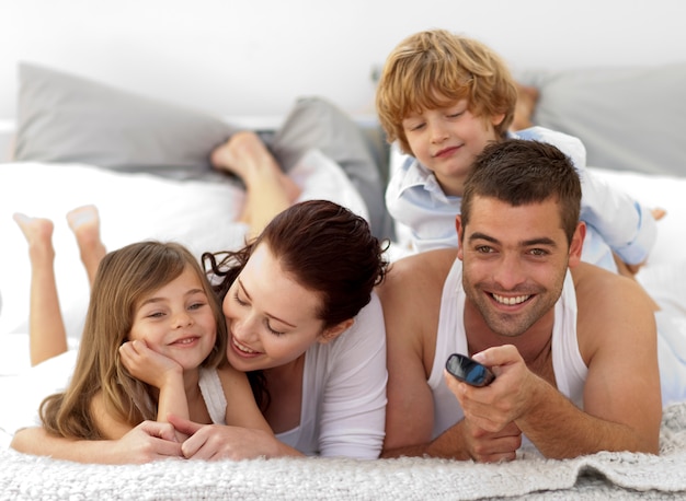 Famiglia sdraiata a letto e usando un telecomando