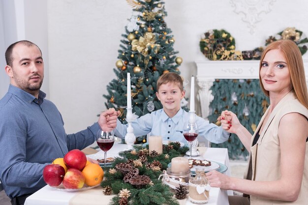 Famiglia seduta a tavola di Natale vicino all'albero di Natale e tenendosi per mano