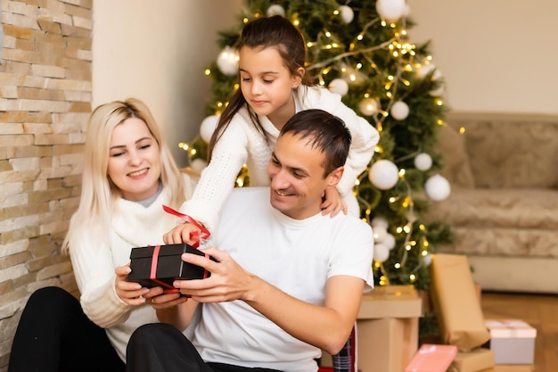 Famiglia seduta su un pavimento. madre, padre e bambina sorridenti vicino all'albero di natale.