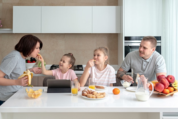 Famiglia sorridente, cenare insieme al tavolo della cucina e divertirsi, genitori con due figlie