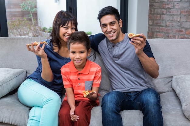 Famiglia sorridente che mangia pizza sul sofà