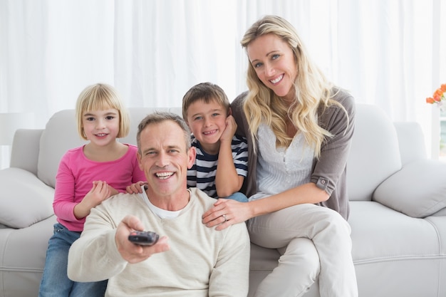 Famiglia sorridente che si siede sul sofà che cambia canale televisivo