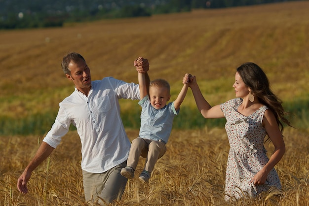 Famiglia sorridente felice che cammina attraverso un campo di grano. Madre, padre e bambino svaghi insieme all'aperto