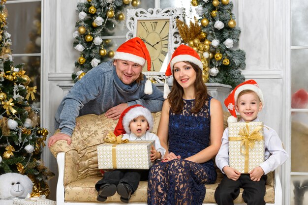 Famiglia sorridente in cappelli dell'assistente di Babbo Natale con molte scatole regalo