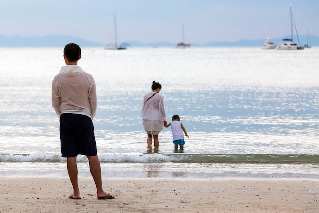Famiglia sul mare. Un padre guarda sua moglie e suo figlio entrare in acqua dalla spiaggia sabbiosa