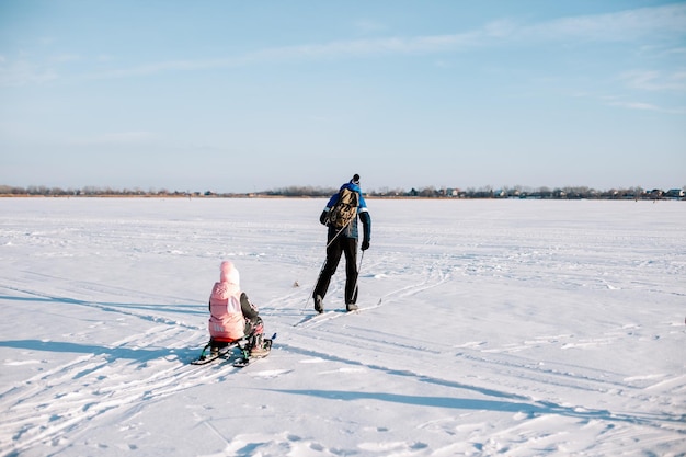 Famiglia sulla passeggiata invernale Giovane uomo e bambino stanno sciando in inverno sul fiume ghiacciato vicino alla foresta l'uomo sta slittando il bambino nella neve