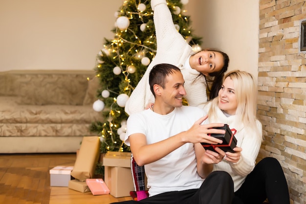 famiglia, vacanze e persone - madre, padre e bambina sorridenti sullo sfondo delle luci dell'albero di Natale